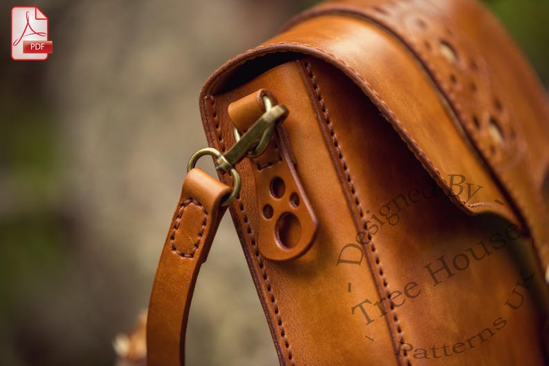 Puede incluir: Primer plano de un bolso de hombro de cuero marr&oacute;n con un patr&oacute;n de puntadas decorativas. El bolso tiene un cierre de solapa con una hebilla de lat&oacute;n y una correa con un anillo de lat&oacute;n. El bolso est&aacute; dise&ntilde;ado por Tree House Patterns.