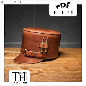 May include: A brown leather kepi hat with a brown leather strap and two brass bullet casings attached to the front. The hat has a brim and a crown. The hat is sitting on a wooden surface. The text "PDF FILES" is visible in the upper right corner of the image.