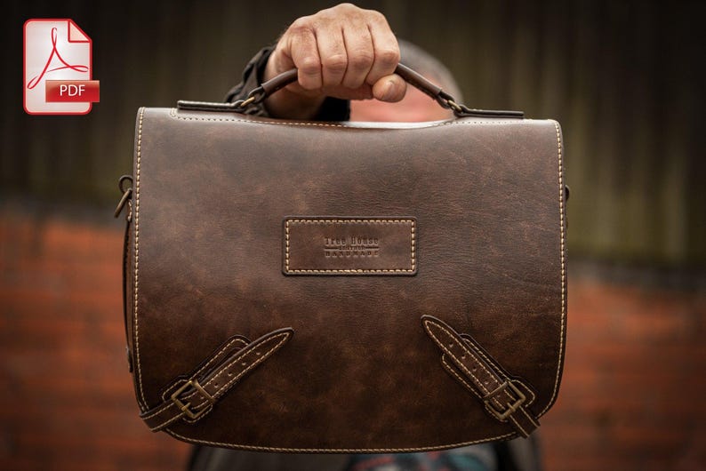 May include: A brown leather briefcase with a top handle and a buckle closure. The briefcase has a small label on the front that reads "The Leather Goods Co."