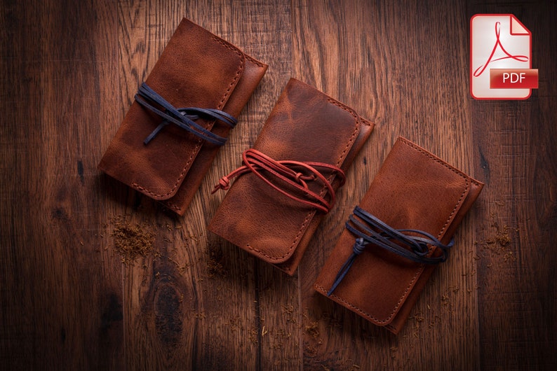 May include: Three brown leather pouches with a flap closure and a tie closure. The pouches are tied with blue and red cords. The pouches are on a wooden surface.