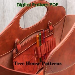May include: A brown leather tote bag with a top handle and multiple pockets inside. The bag is open and you can see the interior pockets. The text "Tree House Patterns" is visible on the bottom of the bag.