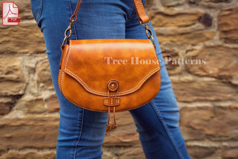 May include: A brown leather crossbody bag with a flap closure and a decorative tassel. The bag has white stitching and a metal buckle. The bag is being worn by a person wearing blue jeans.
