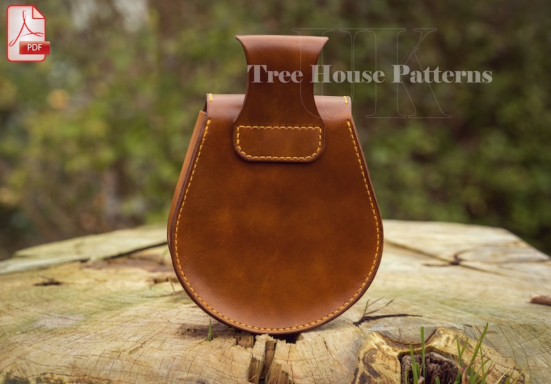 May include: A brown leather pouch with a flap and a handle. The pouch is stitched with yellow thread and has a rustic look. The pouch is sitting on a wooden surface. Tree House Patterns is printed on the pouch.