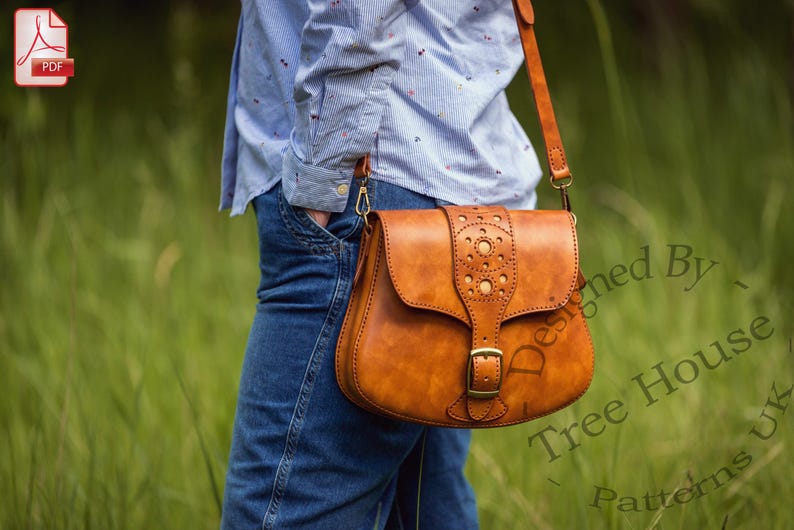 Puede incluir: Un bolso de cuero marr&oacute;n con cierre de solapa y costuras decorativas. El bolso tiene una hebilla y una correa. El bolso lo lleva una persona con una camisa azul y pantalones vaqueros.