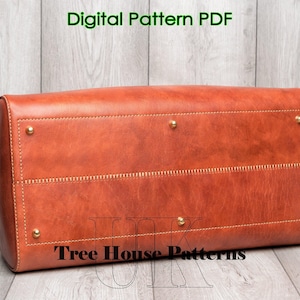 May include: A brown leather tote bag with gold accents and stitching. The bag has a flap closure and a top handle. The bag is sitting on a wooden surface. The text "Tree House Patterns" is visible on the bag.