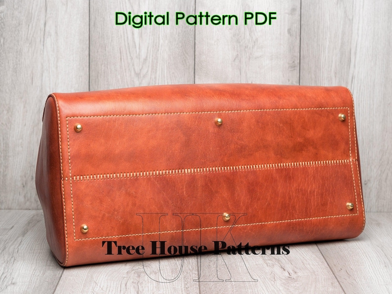 May include: A brown leather tote bag with gold accents and stitching. The bag has a flap closure and a top handle. The bag is sitting on a wooden surface. The text "Tree House Patterns" is visible on the bag.