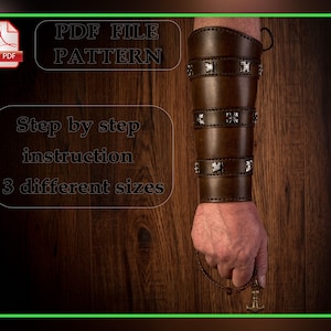 May include: A brown leather arm cuff with silver-colored cross accents. The cuff is shown on a person's arm, holding a pendant. The image also includes text that says "PDF FILE PATTERN", "Step by step instruction", and "3 different sizes".