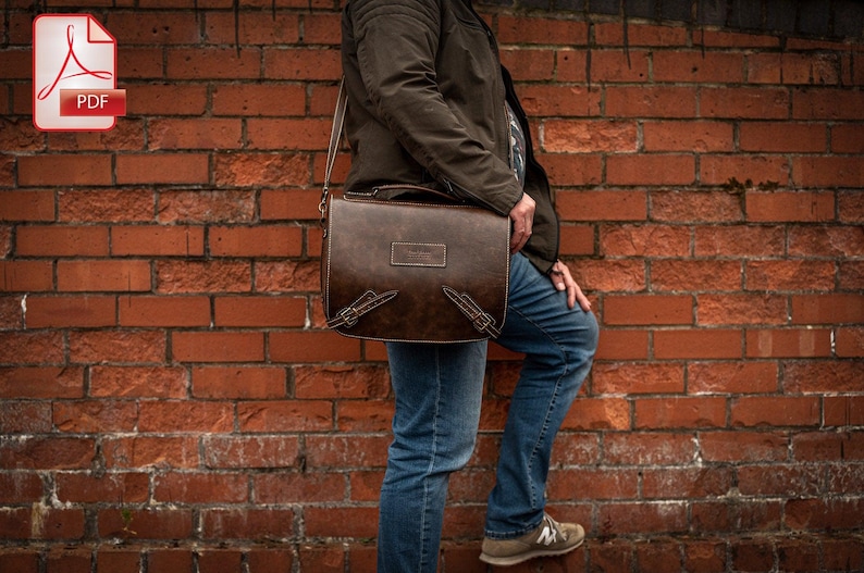 May include: A brown leather messenger bag with a flap closure and adjustable strap. The bag has a distressed look and is being worn by a person standing in front of a brick wall.