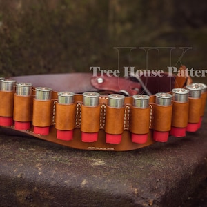 May include: A brown leather shotgun shell belt with 12 shotgun shells. The belt has a red and white stitching detail. The text 'Tree House Patterns' is visible on the belt.