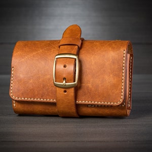May include: A brown leather wallet with a strap and buckle closure. The wallet has a distressed look and is stitched with white thread.