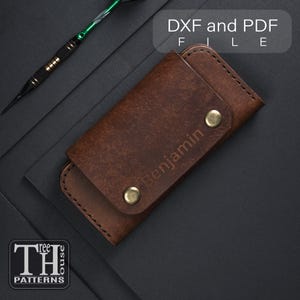 Puede incluir: Un llavero de cuero marrón con el nombre "Benjamin" grabado en relieve en la parte delantera. El llavero se cierra con dos broches de color latón. El texto "DXF and PDF FILE" está en la esquina superior derecha. El logotipo "TH PATTERNS" está en la esquina inferior izquierda.