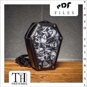 Könnte beinhalten: Schwarze Leder-Koffer-Tasche mit Totenkopf- und Rauchdesign. Die Tasche hat einen Reißverschluss und einen Schultergurt. Die Tasche wird von Three House Patterns hergestellt.