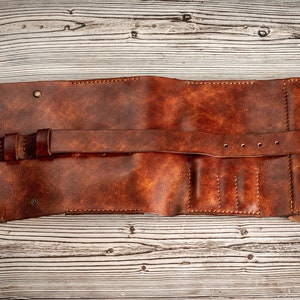 May include: A brown leather wallet with a strap and buckle closure. The wallet has multiple slots for cards and cash.