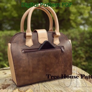 May include: A brown leather handbag with a tan leather trim and a zippered pocket on the back. The bag has a top handle and a flap closure. The text "Tree House Patterns" is visible on the bottom of the bag.