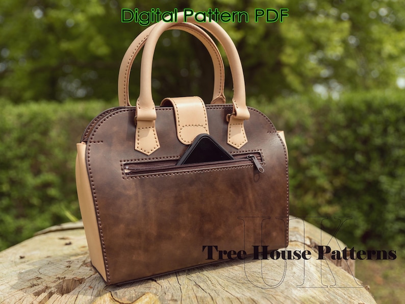 May include: A brown leather handbag with a tan leather trim and a zippered pocket on the back. The bag has a top handle and a flap closure. The text "Tree House Patterns" is visible on the bottom of the bag.
