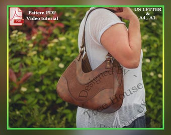 May include: A brown leather handbag with a flap closure and a decorative stitch design. The bag is being worn by a person in a white shirt. The text "Designed by Tree House Patterns UK" is visible on the bag.