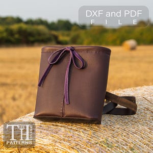Peut inclure: Un sac en cuir marron foncé avec une fermeture à nœud et une sangle violettes. Le sac est posé sur une botte de foin dans un champ. Le texte en haut indique "DXF and PDF FILE". Le logo "TH PATTERNS" est en bas.