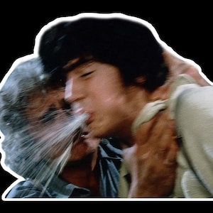以下が含まれることがあります： 2 人が抱き合っているヴィンテージ映画のスチル写真。一人がもう一人にキスをしており、液体の飛沫が見えます。画像には白い境界線と黒い背景があります。