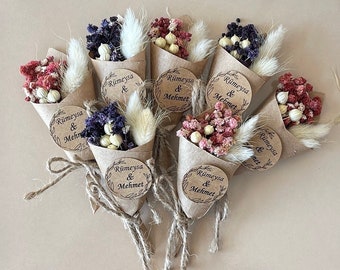 Op de afbeelding: Een verzameling kleine, kegelvormige papieren kegels gevuld met gedroogde bloemen. Elke kegel heeft een bruine papieren cirkel bevestigd met de tekst "Rümeysa & Mehmet" in een cirkelvormig ontwerp.