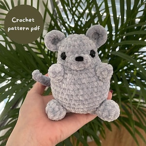 Könnte beinhalten: Ein gehäkeltes graues Maus-Amigurumi-Spielzeug. Das Spielzeug hat schwarze Augen und eine schwarze Nase. Das Spielzeug wird in einer Hand gehalten.