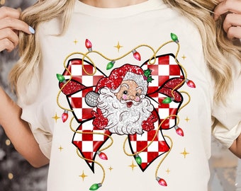 May include: A white t-shirt with a red and white checkered bow with a Santa Claus face in the center. The bow is surrounded by a string of Christmas lights.