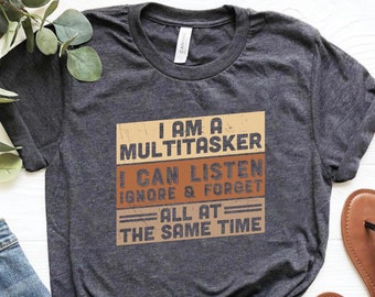 May include: A dark gray t-shirt with a vintage-style graphic that reads "I am a multitasker I can listen ignore & forget all at the same time".