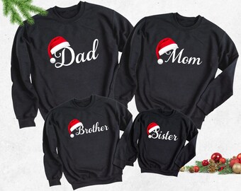 May include: Four black Christmas sweaters with a Santa hat graphic and the words "Dad", "Mom", "Brother", and "Sister" in white.