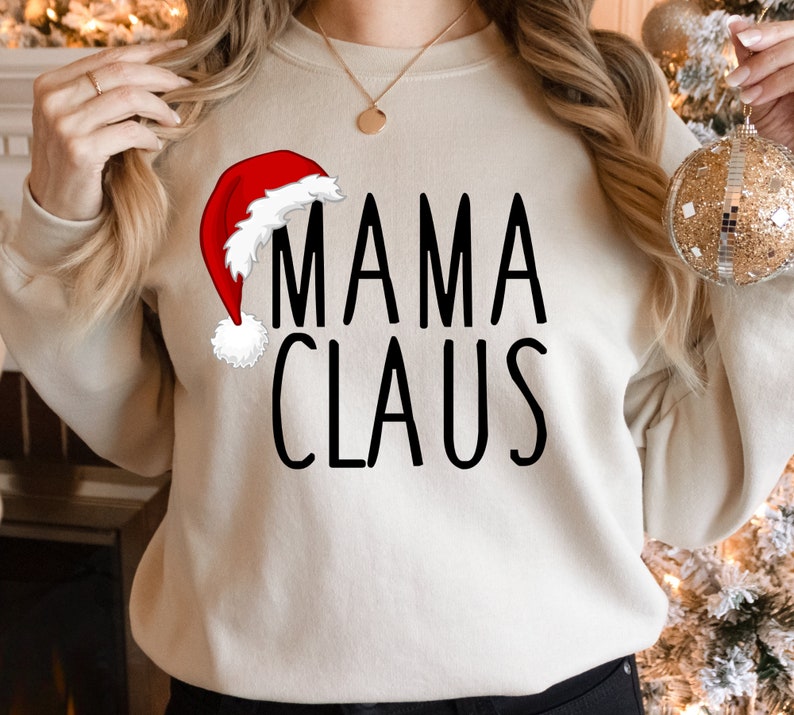 May include: A cream-colored sweatshirt with the text "MAMA CLAUS" in black lettering. A red and white Santa hat is to the left of the text.