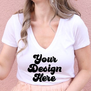 May include: White v-neck t-shirt with the text "Your Design Here" in a retro font.