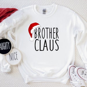 May include: White Christmas sweatshirt with a red Santa hat graphic and the text "Brother Claus".