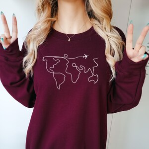 May include: A maroon sweatshirt with a white outline of the world and a small airplane flying above it.