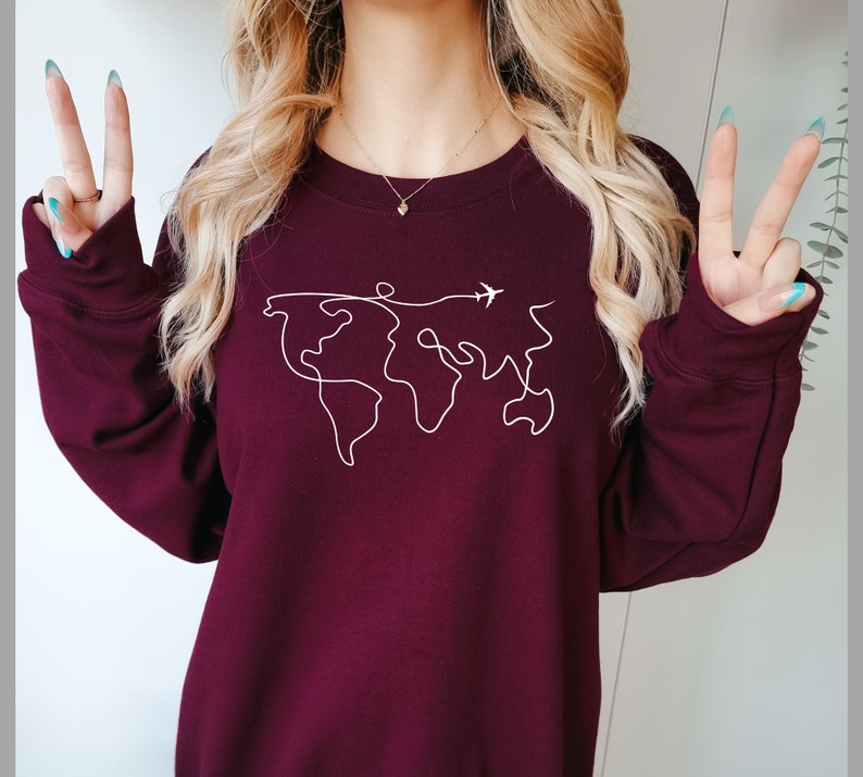 May include: A maroon sweatshirt with a white outline of the world and a small airplane flying above it.