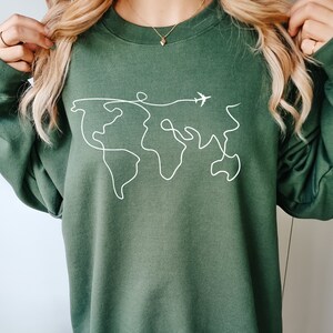 May include: A dark green sweatshirt with a white outline of the world and a small airplane flying above it.