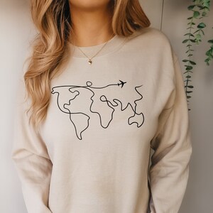 May include: A beige sweatshirt with a black line drawing of the world and a small airplane flying above it.