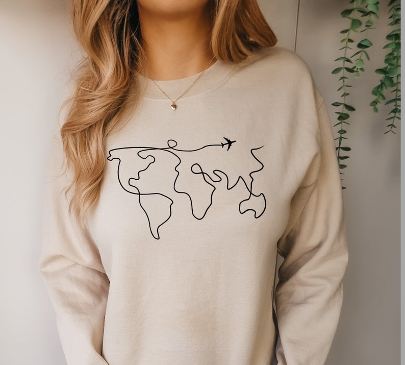 May include: A beige sweatshirt with a black line drawing of the world and a small airplane flying above it.