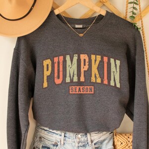 Może przedstawiać: Szara bluza z nadrukiem w stylu vintage z napisem "Pumpkin Season" w kolorach tęczy.