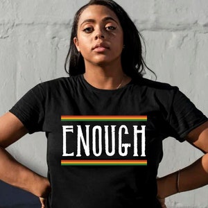 May include: Black t-shirt with the word "ENOUGH" printed in white letters with a red, yellow, and green stripe above and below the word.