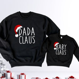 May include: Black Christmas themed sweatshirts with the text "Dada Claus" and "Baby Claus" in white lettering. Each sweatshirt features a red Santa hat graphic.
