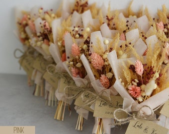 Op de afbeelding: Een verzameling kleine boeketten van gedroogde bloemen, verpakt in roze tissuepapier en vastgebonden met touw. Elk boeket heeft een bruin papieren label met de tekst "Late & Kaan 17.07.2021".