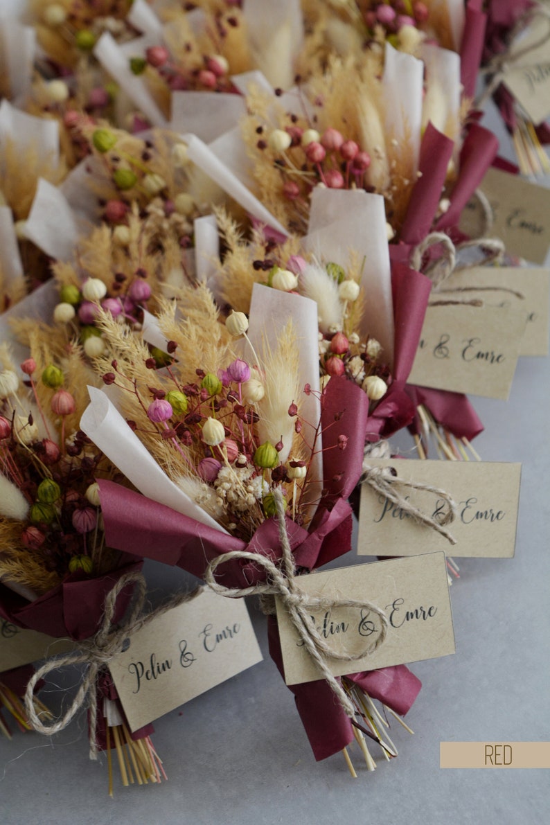 Op de afbeelding: Een verzameling kleine boeketten gedroogde bloemen, verpakt in bordeauxrood papier met een bruin label waarop "Peln & Emre" staat.