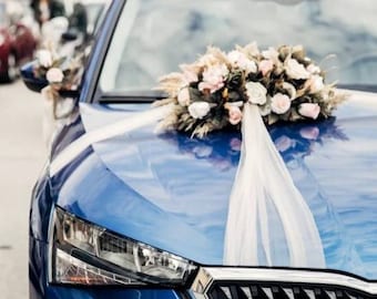 Può includere: Un'auto blu decorata con un nastro di tulle bianco e un bouquet di fiori rosa e bianchi. L'auto ha una griglia nera e una targa che recita "TR 06".
