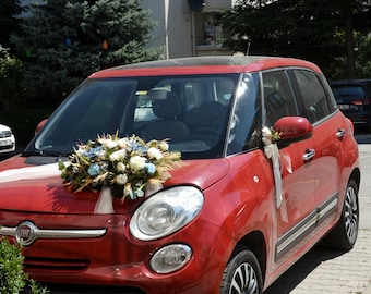 Può includere: Una Fiat 500 rossa decorata con fiori bianchi e blu per un matrimonio. L'auto ha un nastro bianco legato intorno al cofano e un fiocco bianco sullo specchietto laterale.