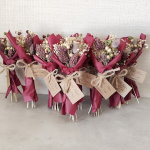 Op de afbeelding: Een groep kleine boeketten gedroogde bloemen, verpakt in bordeauxrood papier met touw en een klein kaartje met de tekst "Bridal Favors" en "Sweet Treats".