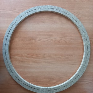 May include: A round, grey, textured ring with small holes around the edge. The ring is on a light brown wooden surface.