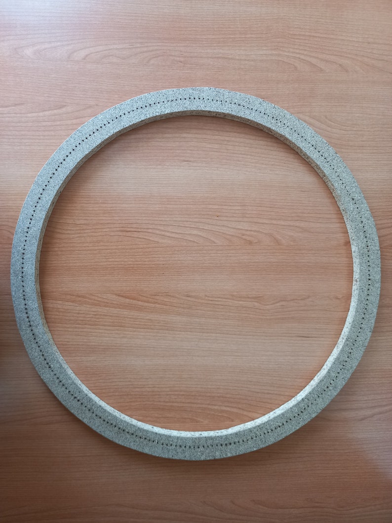 May include: A round, grey, textured ring with small holes around the edge. The ring is on a light brown wooden surface.