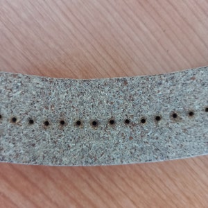 May include: A close-up of a light brown leather watch strap with multiple small holes for adjusting the size.
