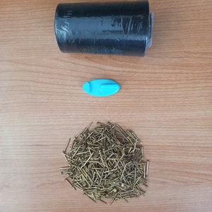 May include: A roll of black shrink wrap, a blue plastic hook, and a pile of gold-coloured tacks on a wooden surface.