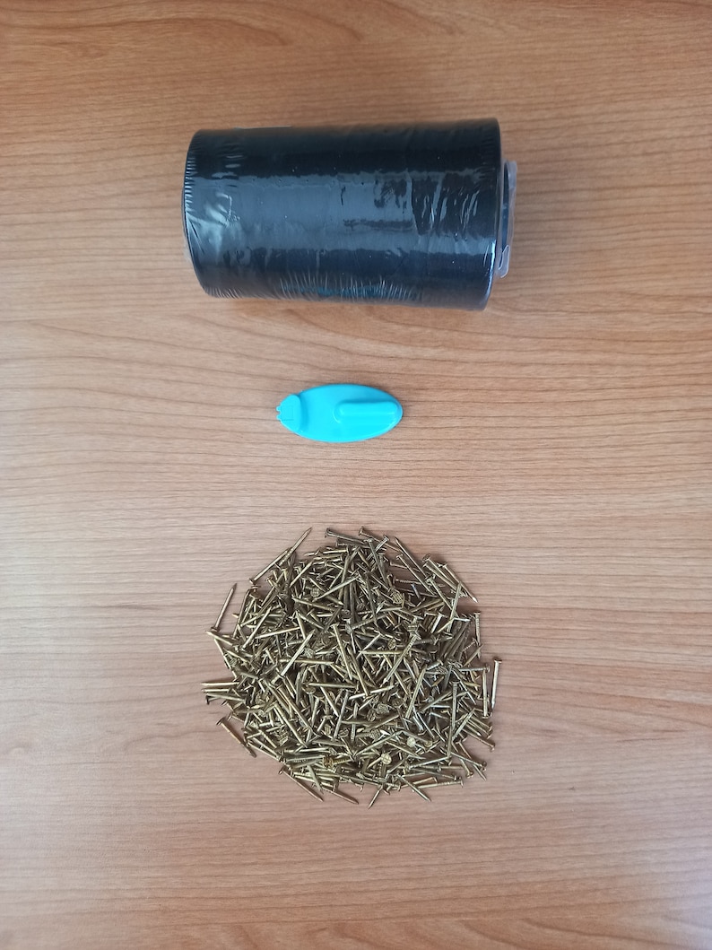 May include: A roll of black shrink wrap, a blue plastic hook, and a pile of gold-coloured tacks on a wooden surface.