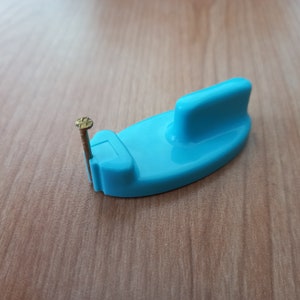 Puede incluir: Un gancho de plástico azul con un pequeño clavo que sobresale del lado.