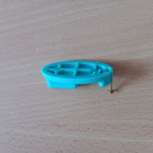 May include: A light blue plastic piece with a grid pattern and a small metal screw. The piece is designed to be attached to a surface.